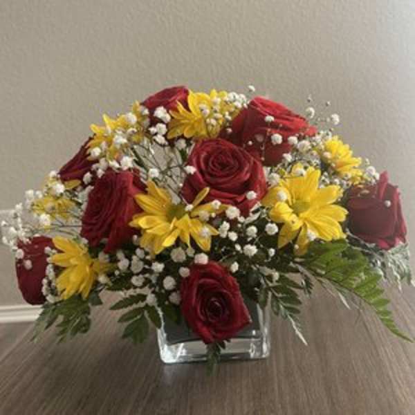 Red roses and yellow daisies in a clear square vase