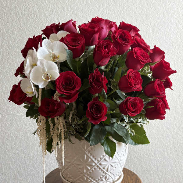 Red roses and white orchids arranged in a white ceramic vase
