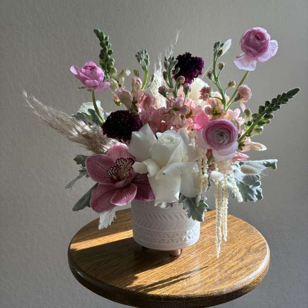 Pink and white floral arrangement in a white vase on a wooden table.