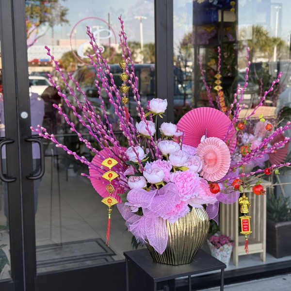 Pink floral arrangement in a gold vase with decorative fans and hanging ornaments