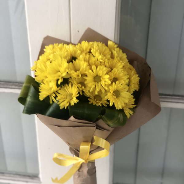 Bouquet of yellow daisies wrapped in brown paper with a yellow ribbon
