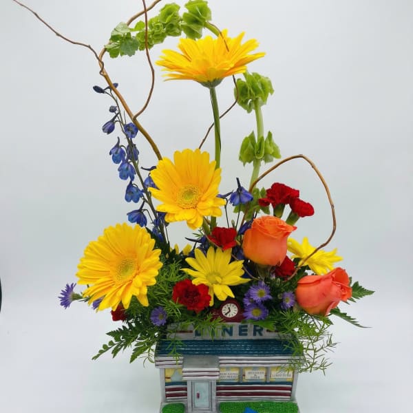 Colorful flower arrangement in a diner-shaped container with a blue toy car