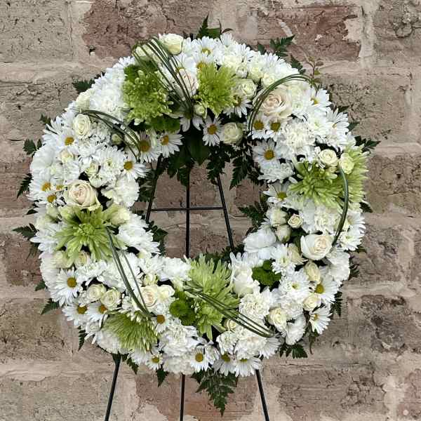 White and green floral wreath on a black stand