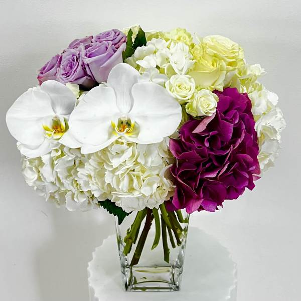 Bouquet of white orchids, hydrangeas, and roses in a clear glass vase