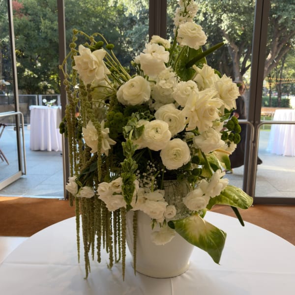 White floral centerpiece in a white vase with trailing greenery