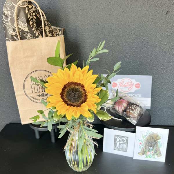 Sunflower arrangement in a glass vase with a gift bag and chocolates