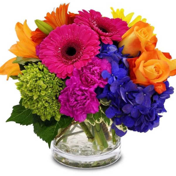 Bright bouquet of pink gerberas, orange roses and lilies, blue hydrangea in a clear glass vase