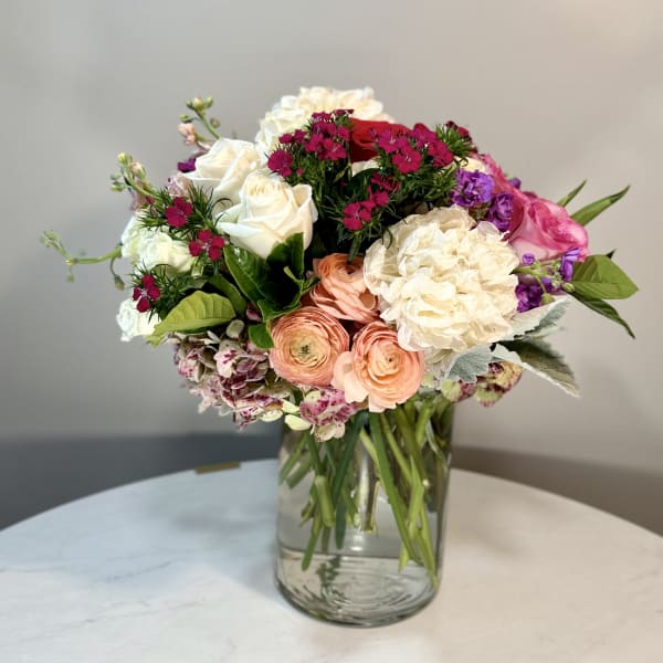 Mixed bouquet of roses, ranunculus, and hydrangeas in a glass vase