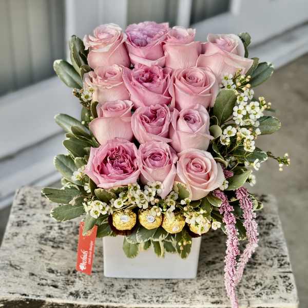 Pink roses arranged in a white square vase with small white filler flowers