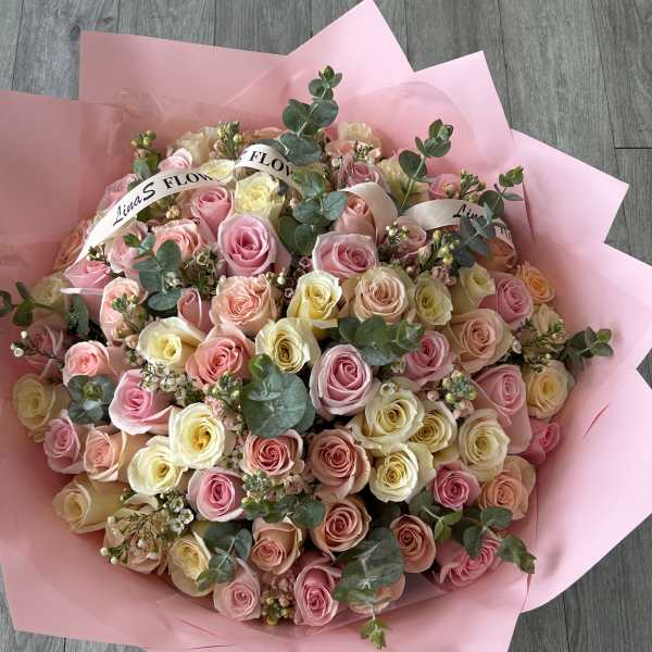 Large bouquet of pink, peach, and cream roses wrapped in pink paper