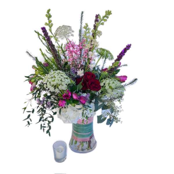 Tall mixed bouquet in a glass vase with a small candle beside it