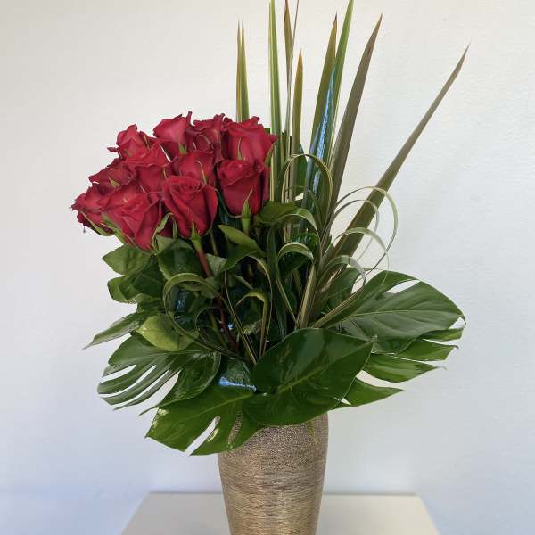 Red roses in a tall gold vase with tropical leaves