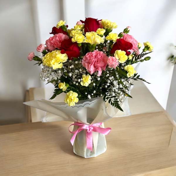Bouquet of red roses, pink carnations, and yellow spray flowers wrapped in white paper