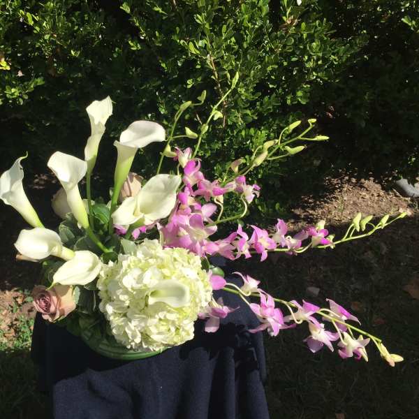 White calla lilies and pink orchids in a low vase with a pale hydrangea bloom