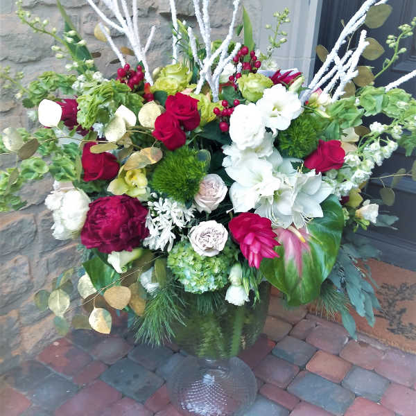 Large mixed floral arrangement in a glass vase with red, white, and green blooms