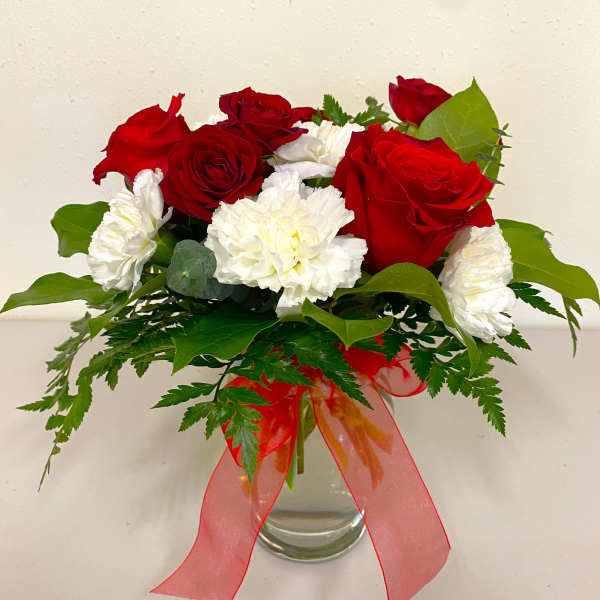 Red roses and white carnations in a glass vase with a red ribbon