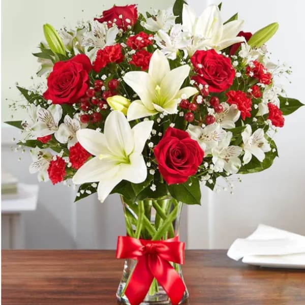 Red roses and white lilies in a glass vase with a red ribbon
