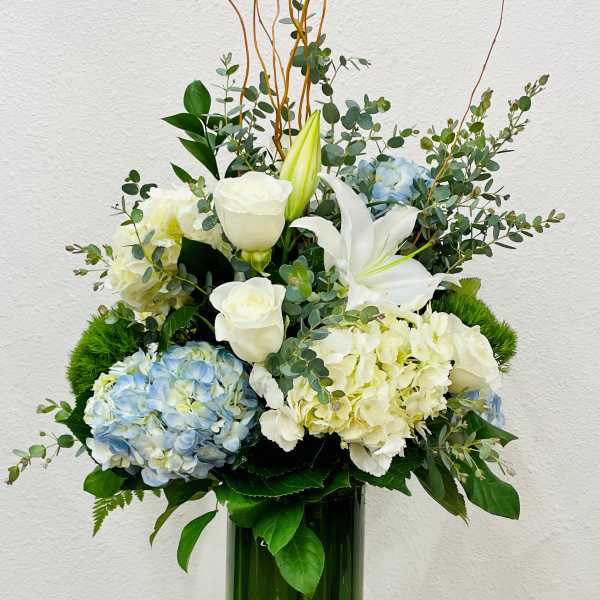White lilies, roses, and blue hydrangeas in a tall green vase