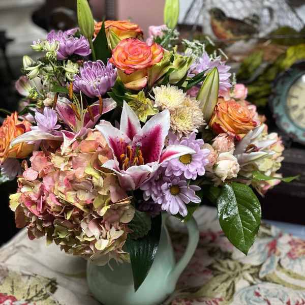Mixed bouquet of roses, lilies, hydrangea, and daisies in a pale vase