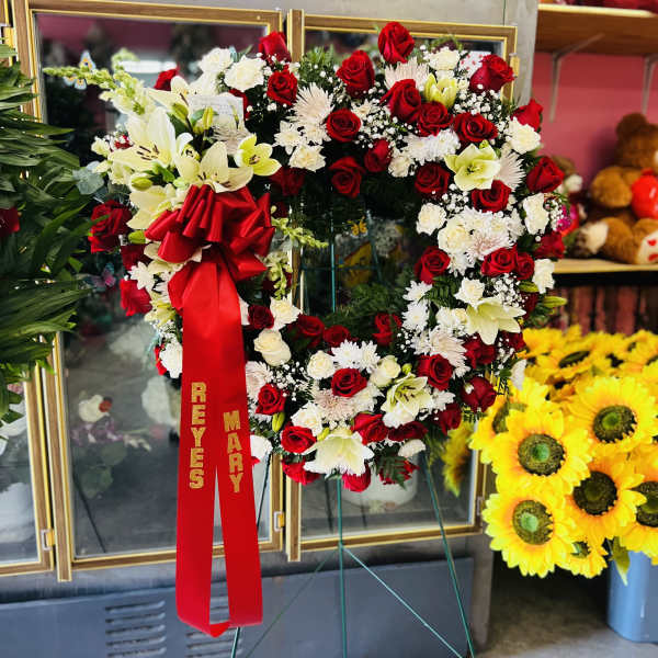 Standing wreath of red roses, white mums, and lilies with a red bow and name ribbon on an easel