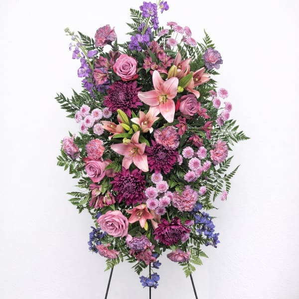 Standing floral spray with pink and purple flowers on a black easel