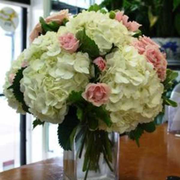 White hydrangea bouquet with pink roses in a clear glass vase