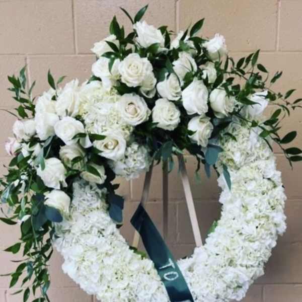 White floral funeral wreath on an easel with a memorial ribbon