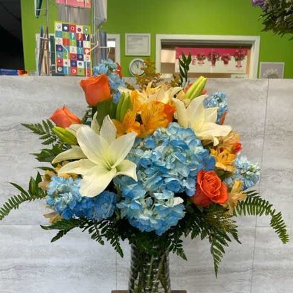 Bouquet of blue hydrangeas, white lilies, and orange roses in a glass vase