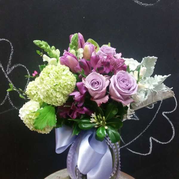 Lavender roses and purple flowers in a glass vase with a ribbon