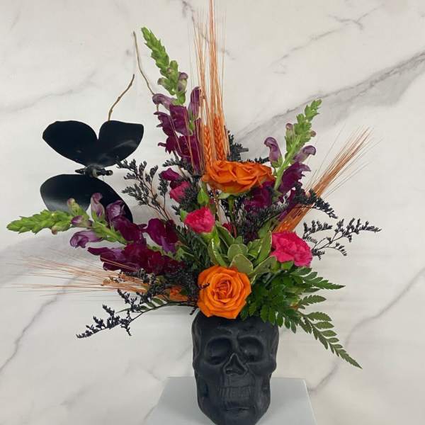 Orange and purple floral arrangement in a black skull vase