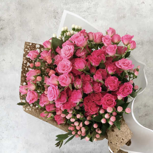 Bouquet of pink roses and berry-like accents wrapped in paper