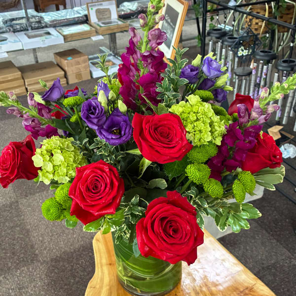 Bouquet of red roses, purple lisianthus, and green hydrangea in a glass vase