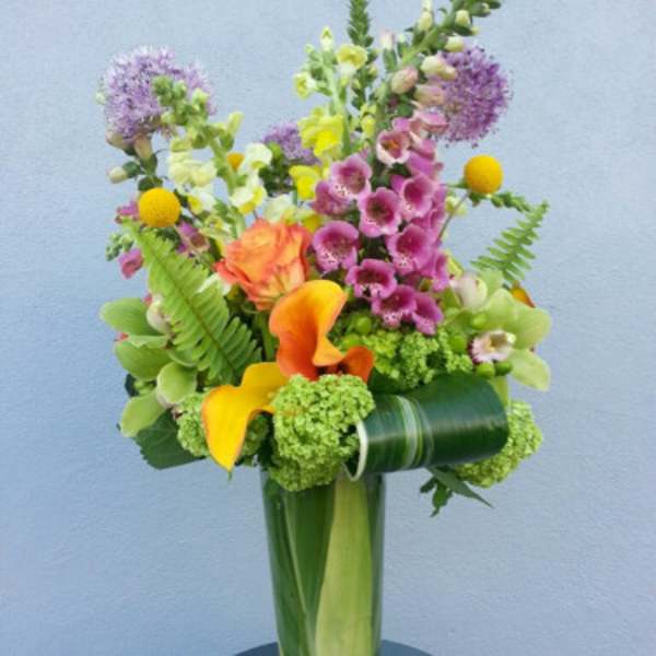 Colorful bouquet with orange calla lilies and purple blooms in a tall glass vase