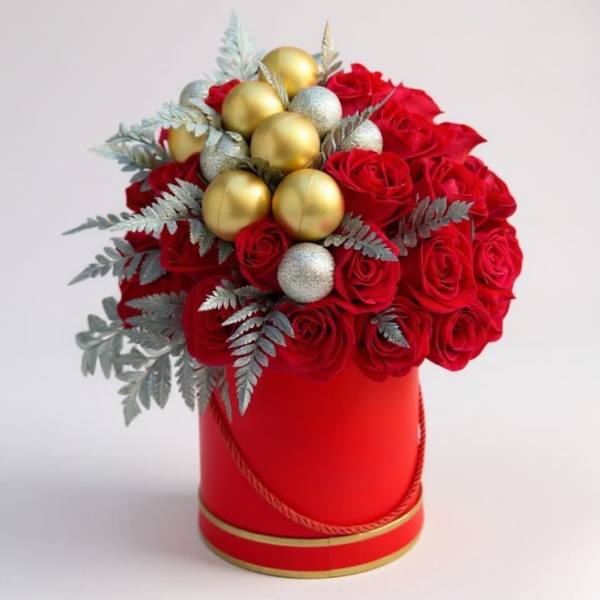 Red roses arranged in a red hat box with gold ornaments and silver foliage