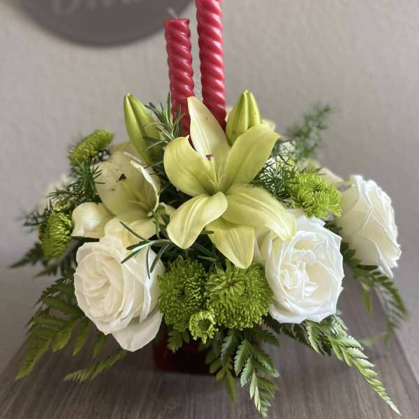 White roses and pale yellow lilies arranged with red candles.