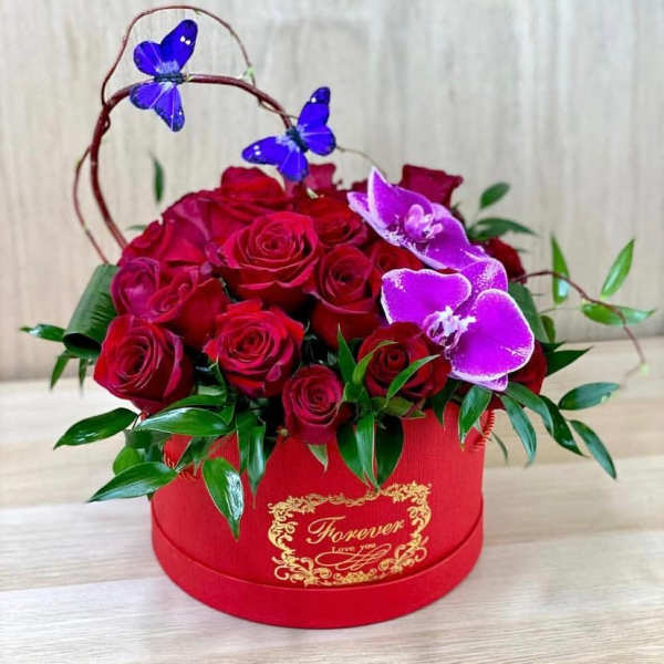 Red roses in a red round box with purple orchid accents
