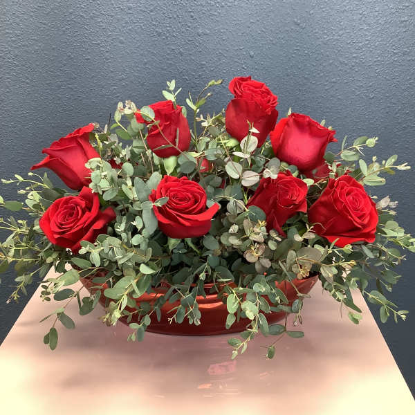 Red roses arranged in a low red container with eucalyptus foliage