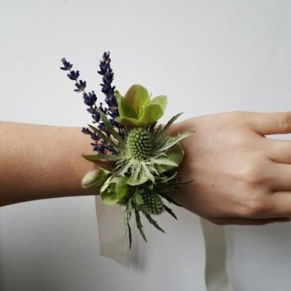 Wrist corsage with green textured blooms and small purple sprigs on a cream ribbon