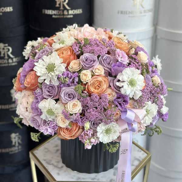 Round bouquet of roses, daisies, and purple filler flowers in a black vase