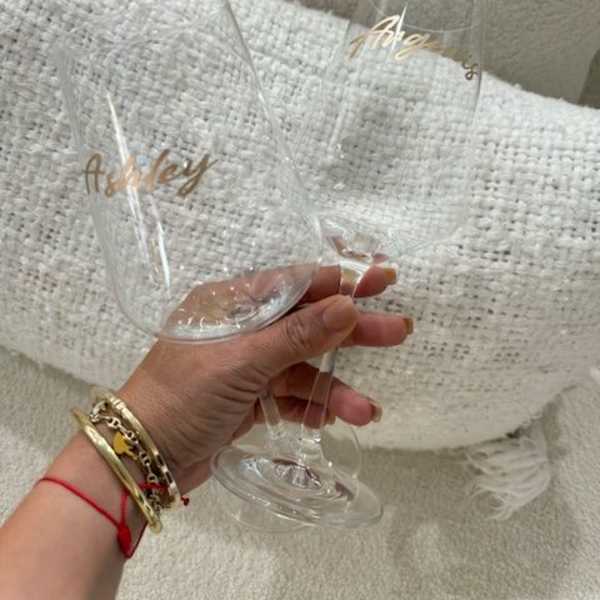 Two clear champagne flutes with gold script lettering held in a hand