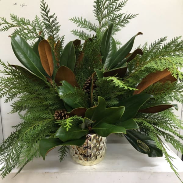 Green holiday arrangement in a gold textured vase with pinecones