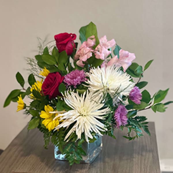 Mixed bouquet of roses, daisies, and pink blooms in a glass vase
