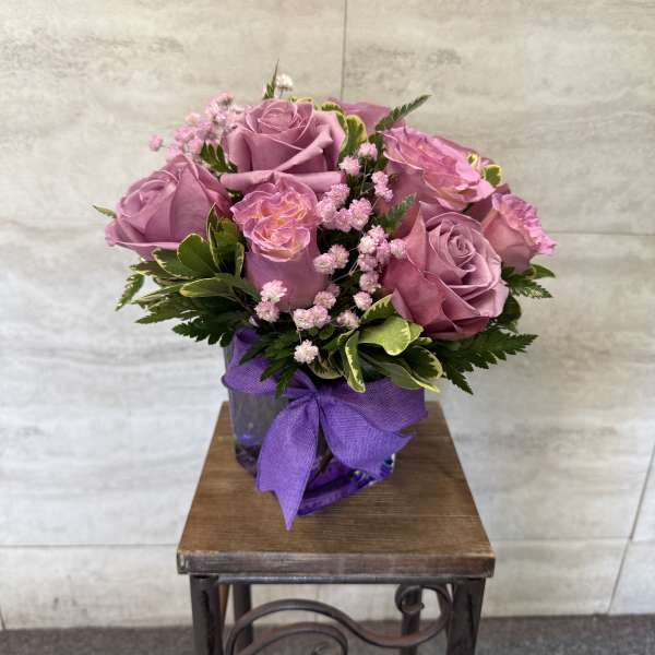 Pink roses in a purple vase with a ribbon bow
