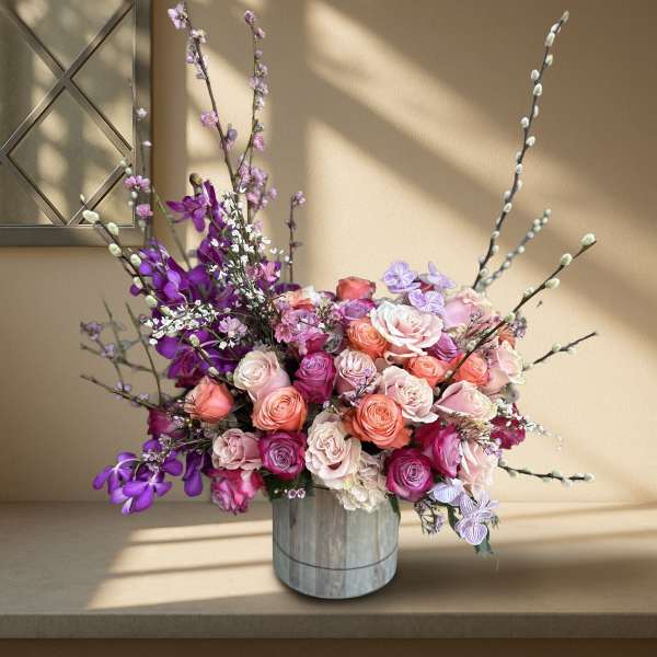 Mixed pink and purple roses in a gray vase with tall branches