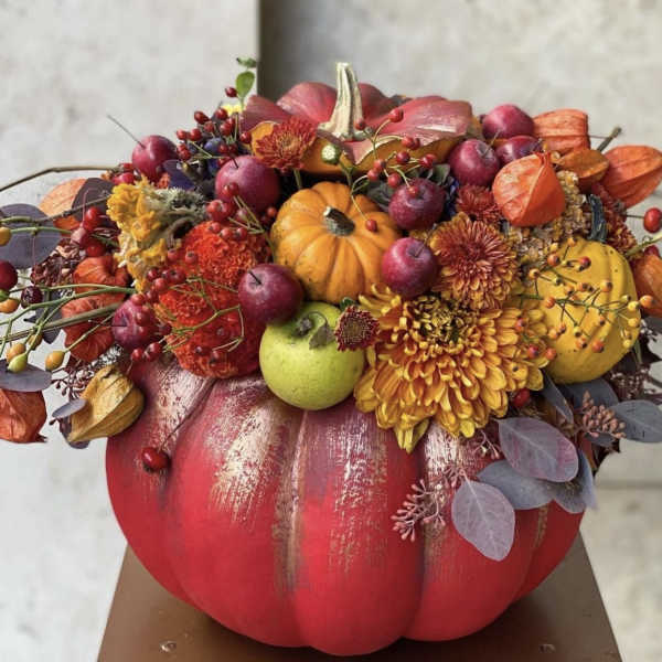 Fall floral arrangement in a painted pumpkin with small pumpkins and berries