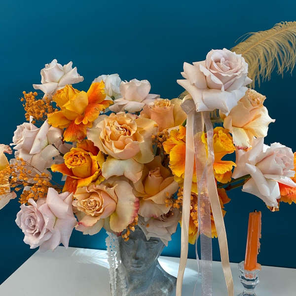 Peach and white roses with orange flowers in a bust vase