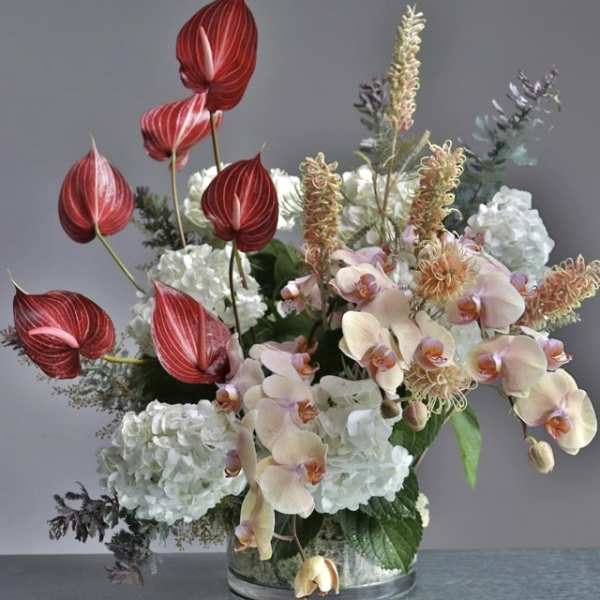 Mixed floral arrangement with red anthuriums, pale orchids, and white hydrangeas in a glass vase
