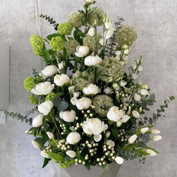 Tall white floral arrangement with green accents in a gray container