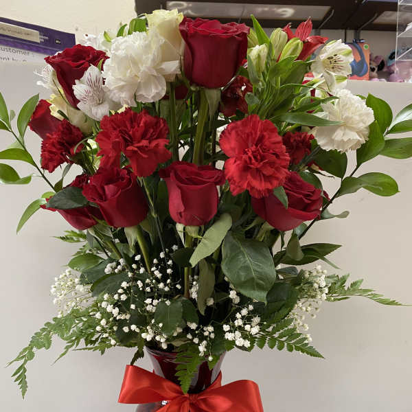 Tall arrangement of red roses and carnations with white blooms in a red vase with a red bow