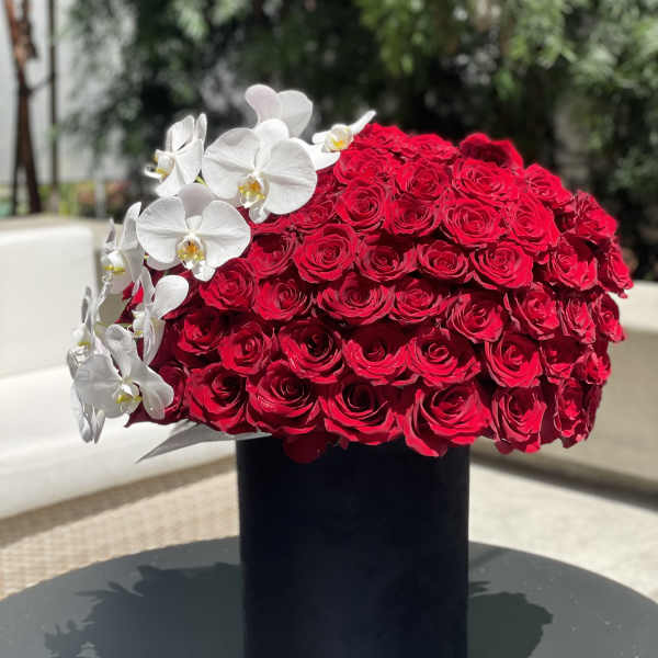 Large red rose arrangement with white orchids in a black vase